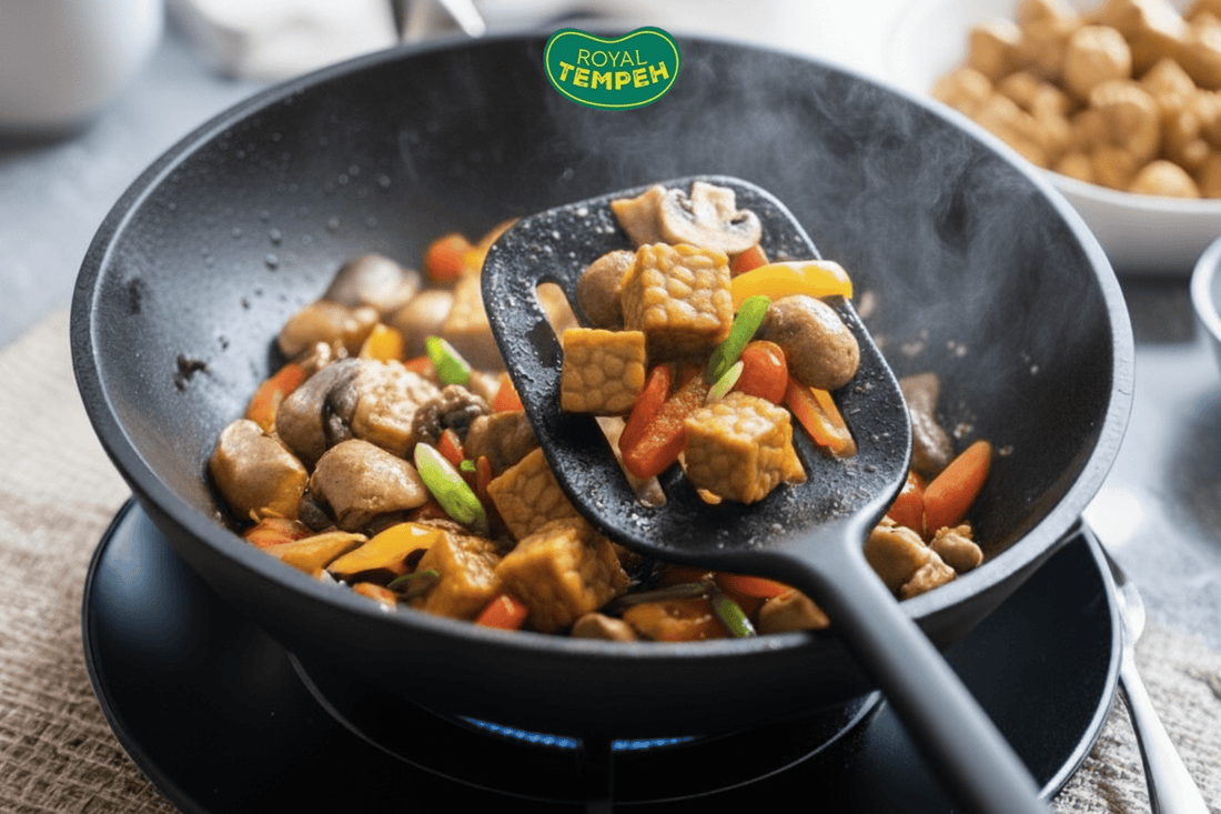 Close-up of tempeh cubes being stir-fried with colorful vegetables and mushrooms in a wok, with steam rising and the Royal Tempeh logo above.