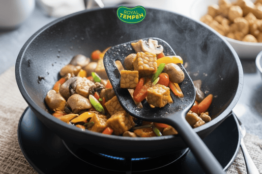 Close-up of tempeh cubes being stir-fried with colorful vegetables and mushrooms in a wok, with steam rising and the Royal Tempeh logo above.