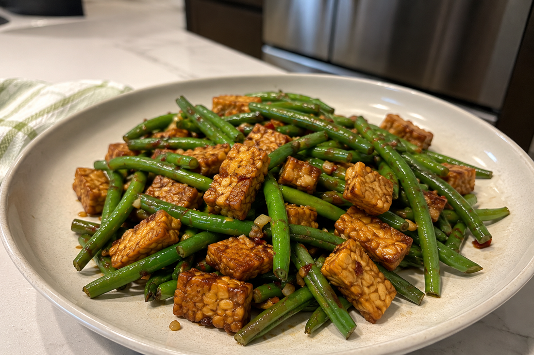 A white plate filled with a savory green bean saute and golden-brown pan-seared tempeh cubes tossed in a garlic glaze.
