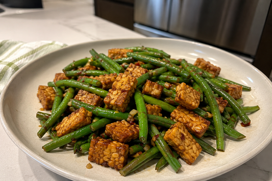 A white plate filled with a savory green bean saute and golden-brown pan-seared tempeh cubes tossed in a garlic glaze.