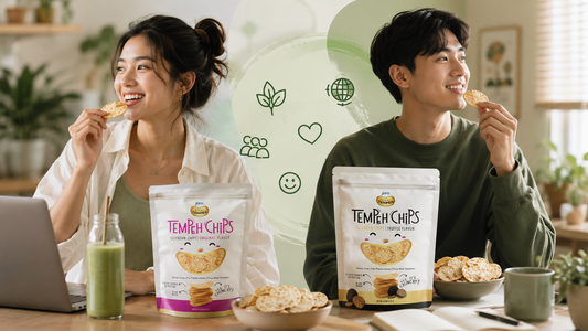 A young man and woman smiling and enjoying crispy tempeh chips at a table with bags of Jans Tempeh Chips and green lifestyle icons in the background.
