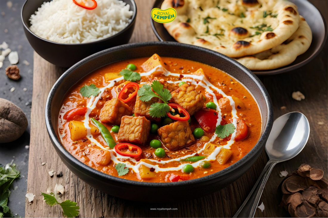 Royal Tempeh curry bowl with tempeh cubes, peas, and vegetables in rich red sauce, served with naan bread and rice.