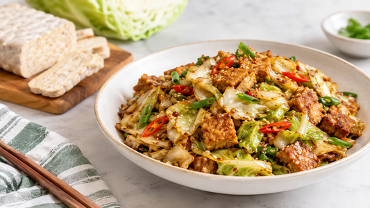 A large bowl of crunchy tempeh salad filled with mixed greens, shredded cabbage, carrots, cucumbers, and seasoned seared Royal Tempeh cubes, set on a light wooden table with a banner reading "A Crunchy Tempeh Salad Recipe That Makes Tempeh the Star.