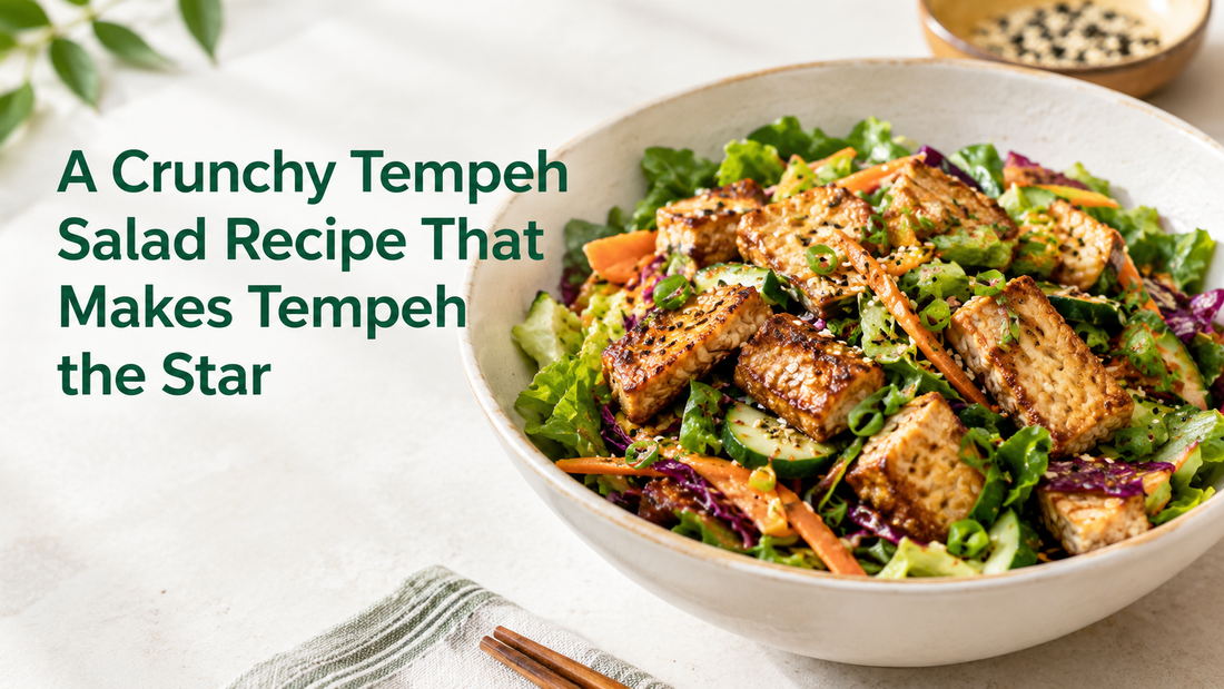 A large bowl of crunchy tempeh salad filled with mixed greens, shredded cabbage, carrots, cucumbers, and seasoned seared Royal Tempeh cubes, set on a light wooden table with a banner reading "A Crunchy Tempeh Salad Recipe That Makes Tempeh the Star.