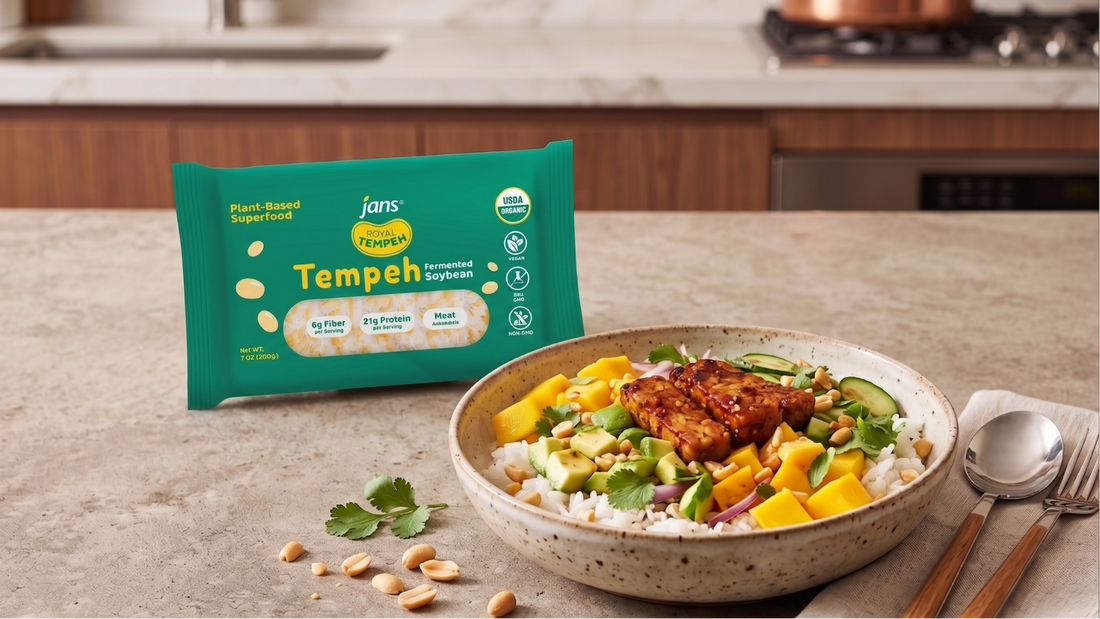 A vibrant ceramic bowl filled with fluffy rice, pan-seared golden tempeh strips, diced fresh mango, chopped cucumbers, and crushed peanuts, sitting next to a green package of Jans Royal Tempeh.