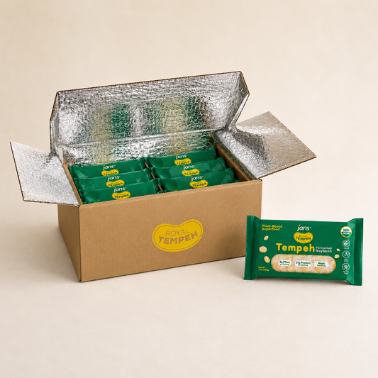 An open cardboard shipping box lined with foil thermal insulation packed with green packages of Royal Tempeh, standing next to an upright green tempeh package on a neutral background.