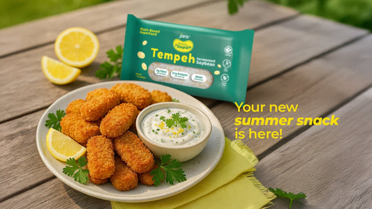 A white plate piled with golden-brown breaded tempeh nuggets, served with lemon slices and a side of creamy white dipping sauce next to a green pack of Jans Royal Tempeh under a "Your new summer snack is here!" text graphic.