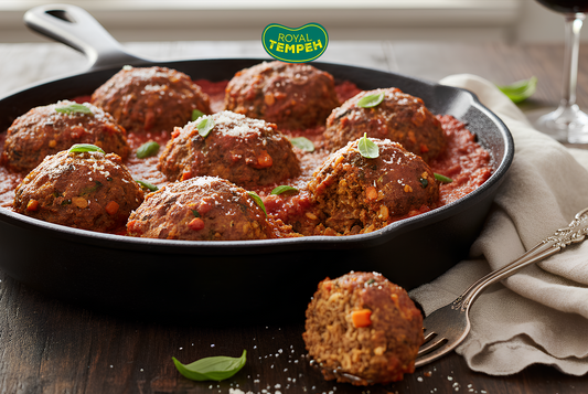 Tempeh meatballs in tomato sauce served in a cast iron skillet, garnished with fresh basil and grated cheese, with the Royal Tempeh logo above.