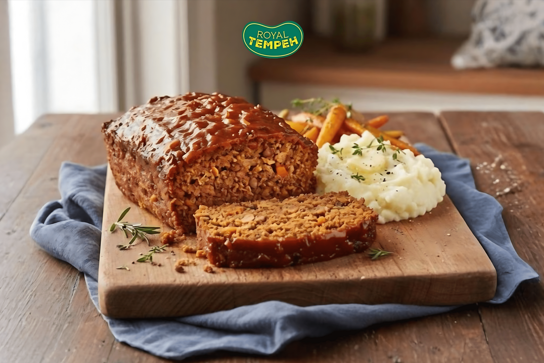 Tempeh loaf glazed with sauce, served with mashed potatoes and roasted carrots on a wooden board, with the Royal Tempeh logo above.