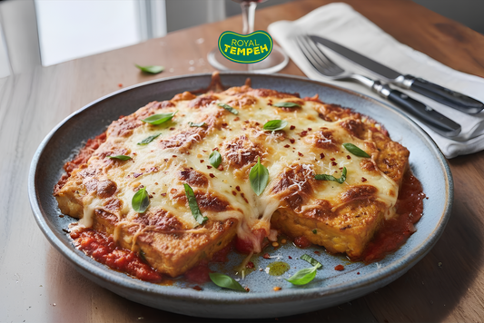 Tempeh parmesan baked in marinara sauce and topped with melted cheese, garnished with fresh basil, served on a ceramic plate with utensils in the background.
