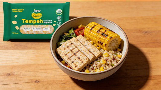 A vibrant meal bowl featuring grilled Royal Tempeh slabs and a cob of charred corn, served over grains and greens next to a green package of Royal Tempeh.