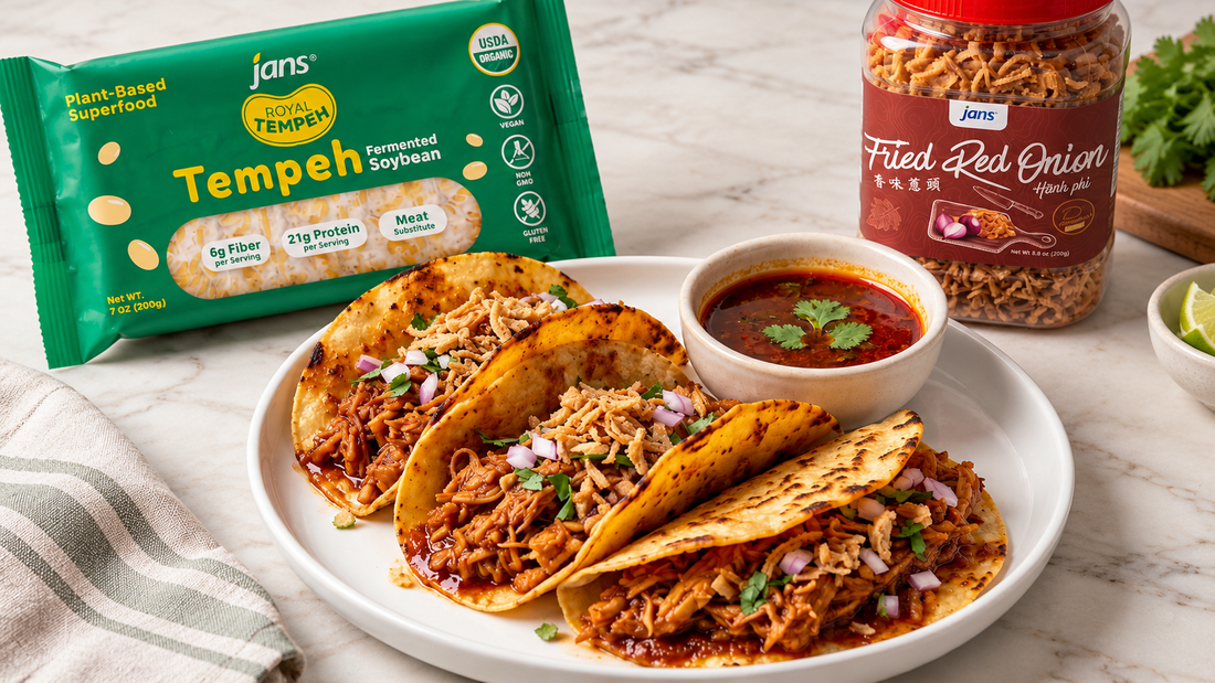 A plate of savory vegan tempeh tacos garnished with red onion and fresh herbs, served alongside a package of Royal Tempeh and a jar of Jans Fried Red Onion.