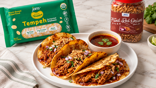 A plate of savory vegan tempeh tacos garnished with red onion and fresh herbs, served alongside a package of Royal Tempeh and a jar of Jans Fried Red Onion.