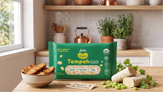 A package of Jans Royal Tempeh Fermented Soybean displayed on a kitchen counter next to a bowl of golden grilled tempeh strips, a raw un-marinated tempeh block, and scattered green edamame soybeans.