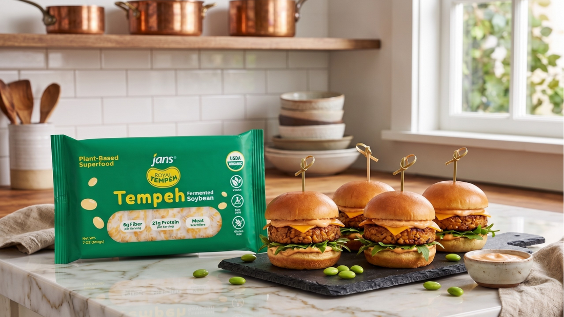 Three mini tempeh burger sliders skewered with bamboo picks on a dark serving slate, positioned in a bright kitchen next to a green package of Jans Royal Tempeh Fermented Soybean and loose green edamame.