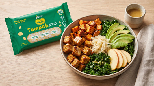 A nourish bowl filled with roasted maple-mustard tempeh cubes, massaged kale, sliced avocado, apple slices, and sauerkraut next to a package of Jans Royal Tempeh Fermented Soybean.