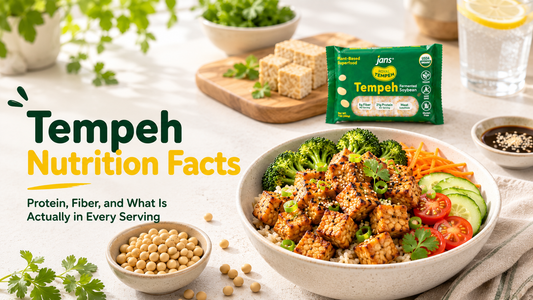 A healthy grain bowl topped with savory cubed tempeh and fresh veggies on a wooden table next to a green package of Jans Tempeh, with graphic text overlay reading "Tempeh Nutrition Facts: Protein, Fiber, and What Is Actually in Every Serving".