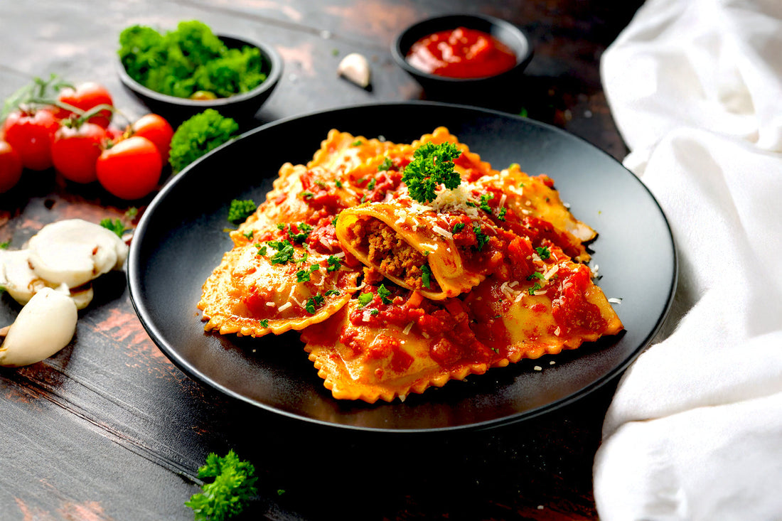 Plate of ravioli topped with tomato sauce, parsley, and grated cheese, surrounded by fresh tomatoes, garlic, and herbs.