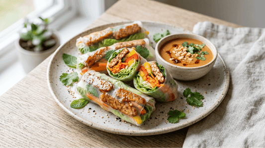 A plate of three translucent fresh tempeh rice paper rolls filled with Royal Tempeh, herbs, and shredded vegetables, served with a creamy peanut dipping sauce.