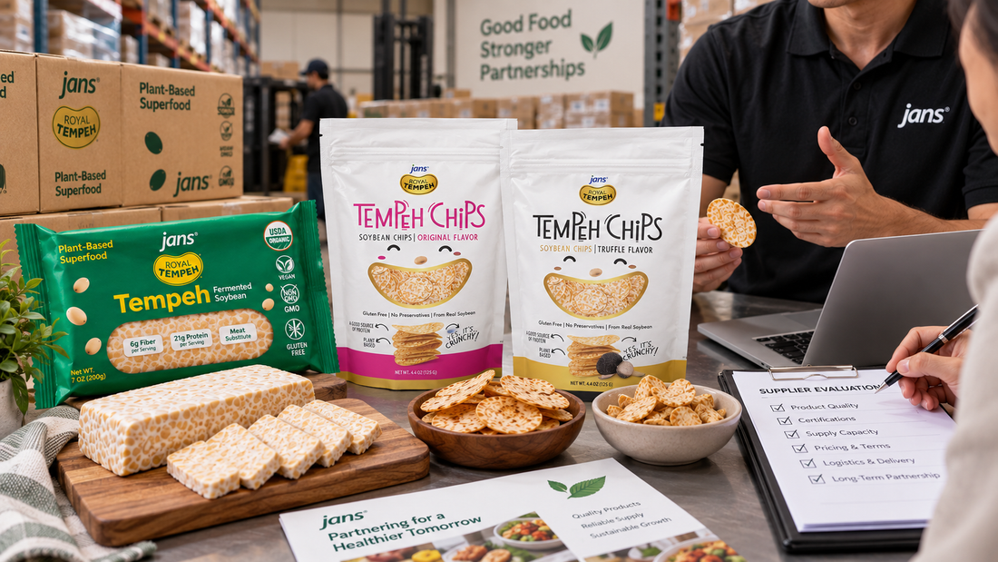A B2B product showcase table with Jans Royal Tempeh packages, sliced fresh tempeh, bags of Tempeh Chips, and professionals reviewing a supplier evaluation checklist in a warehouse.