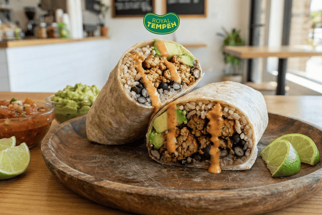 Royal Tempeh burrito with rice beans avocado and sauce on wooden plate.