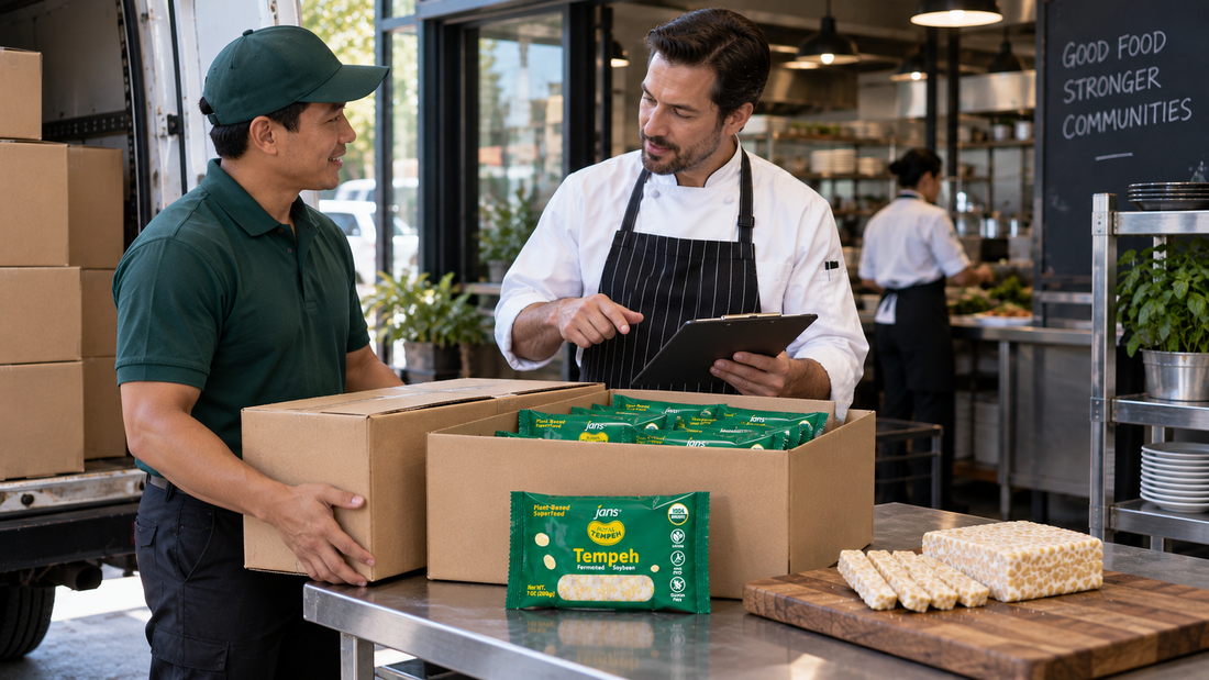 A delivery worker and a chef inspecting bulk shipments of packaged Royal Tempeh boxes and fresh slices on a kitchen prep table.