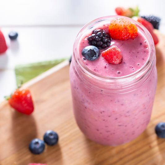 A thick, vibrant purple Tempeh Very Berry Smoothie served in a clear glass mason jar, topped with fresh strawberries, blueberries, and blackberries, resting on a wooden board.