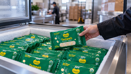 A warehouse worker's hand organizing and stocking a commercial freezer chest filled with neatly arranged packages of Royal Tempeh.