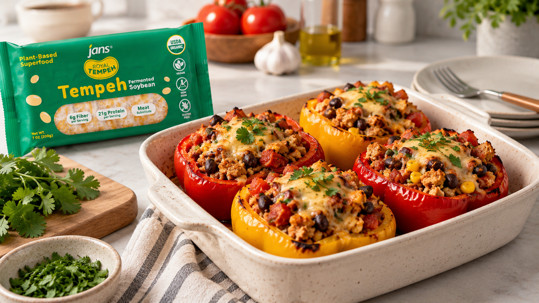 A baking dish of vibrant roasted red and yellow bell peppers stuffed with a savory tempeh and grain filling, garnished with fresh cilantro, alongside a package of Royal Tempeh.