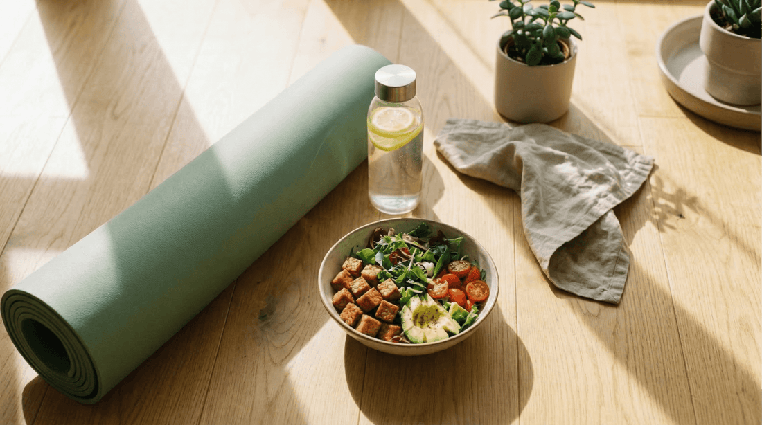 A fitness-themed setting featuring a rolled yoga mat, a water bottle, and a healthy bowl of Royal Tempeh and fresh vegetables on a sunny wooden floor.